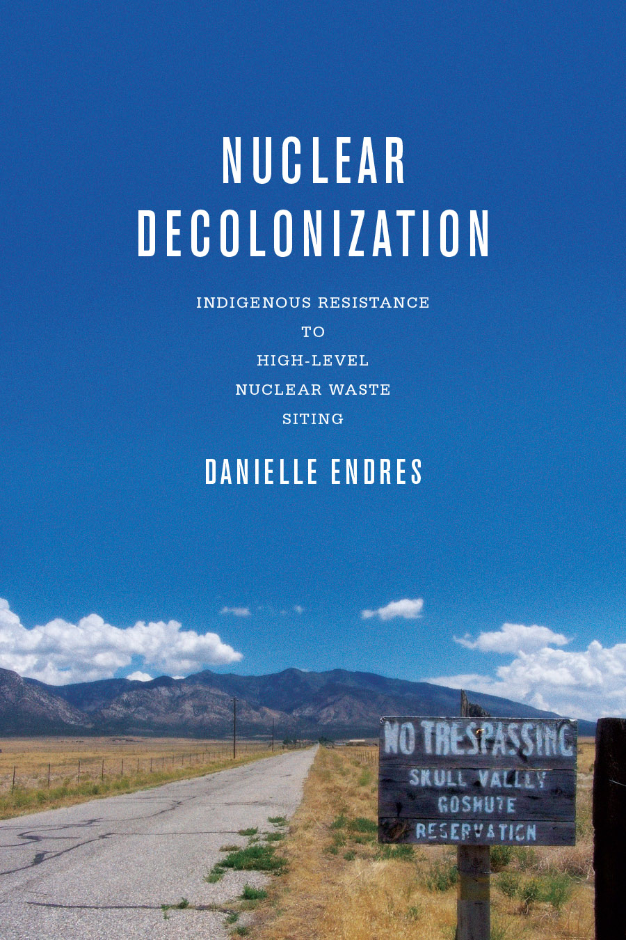 Front cover of Nuclear Decolonization: Indigenous Resistance to High-Level Nuclear Waste Siting, by Danielle Endres, featuring a photograph of a far-off mountain with a cracked asphalt road leading to it, with a sign in the foreground reading No Trespassing. Skull Valley Goshute Reservation.